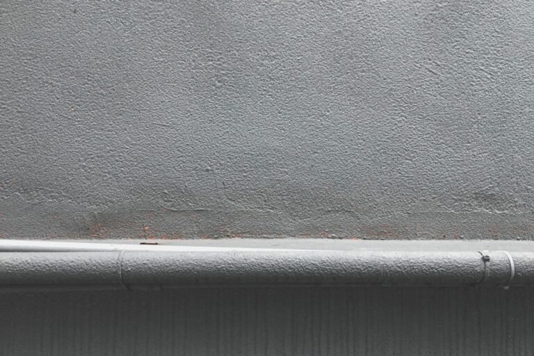 Close-up of a textured grey concrete wall with a metal pipeline along the bottom edge.
