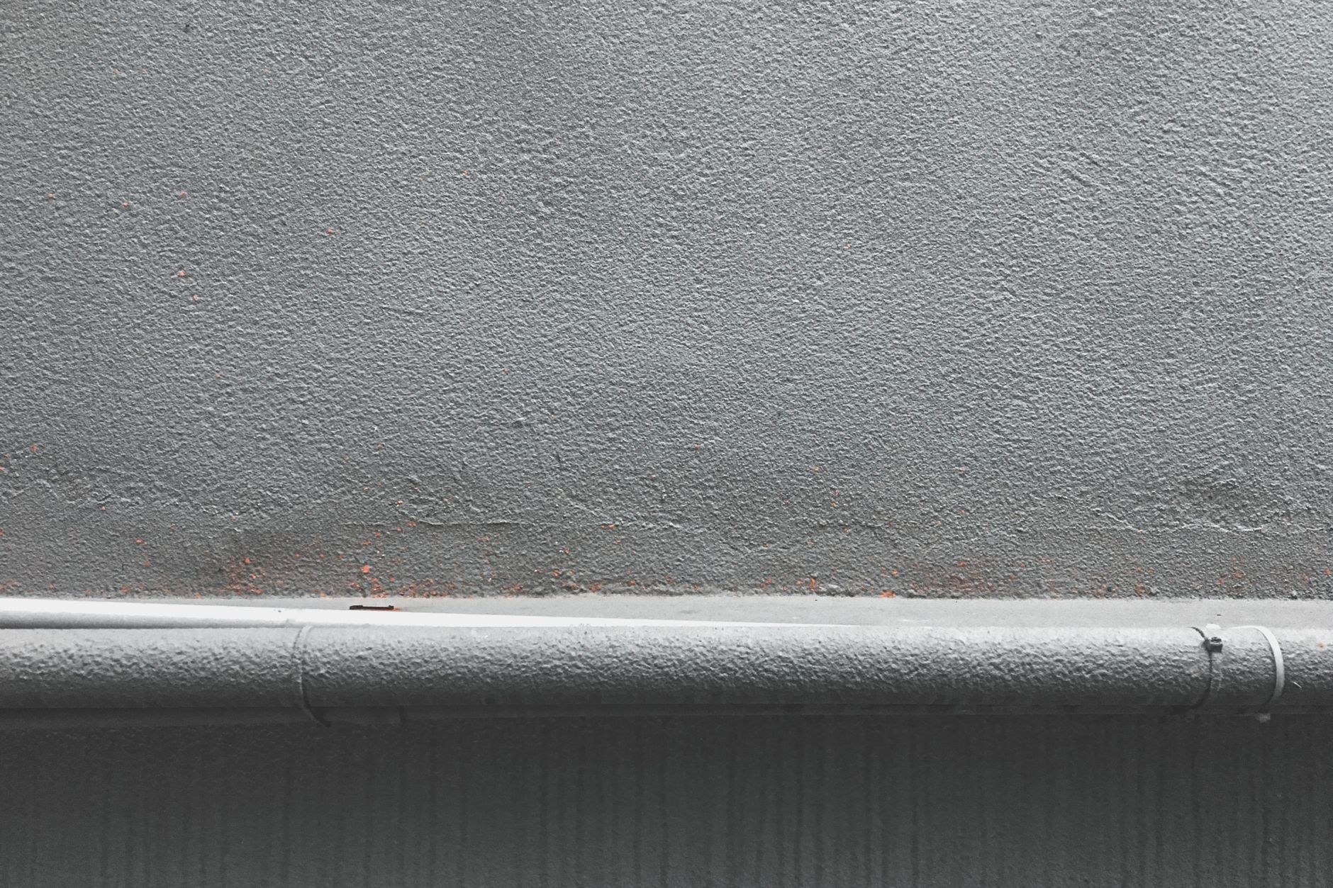 Close-up of a textured grey concrete wall with a metal pipeline along the bottom edge.