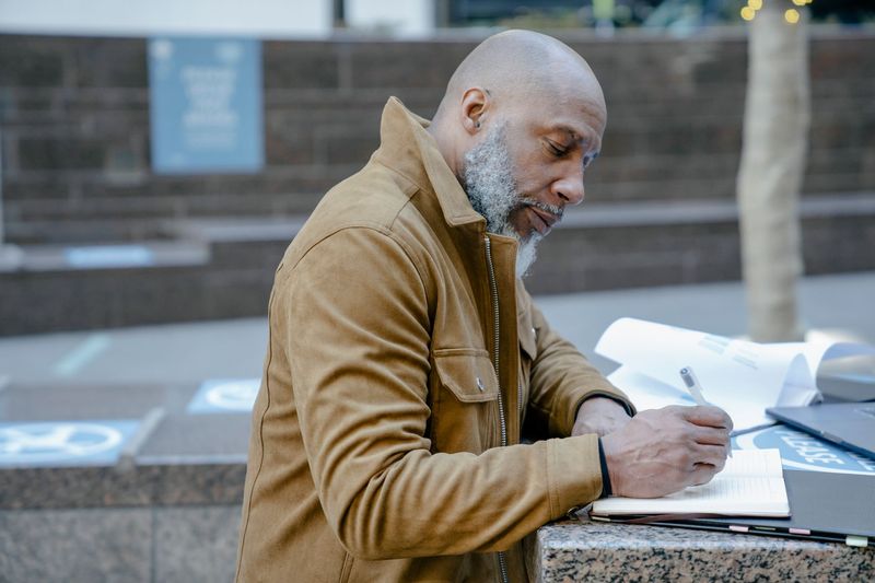 Man writing in a pocket notebook on a city ledge, everyday carry in an urban setting