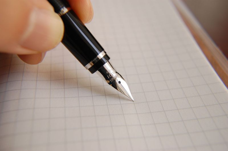 Fountain pen nib touching graph paper, testing ink bleed-through and paper quality