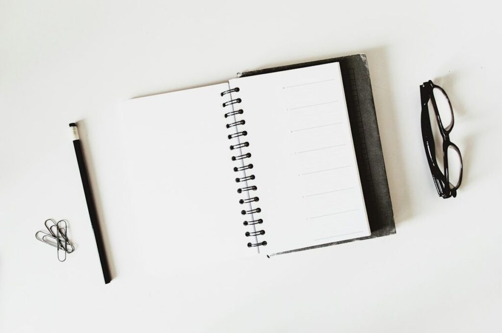 Notebook, pen, and glasses laid out on a desk representing nurse EDC essentials