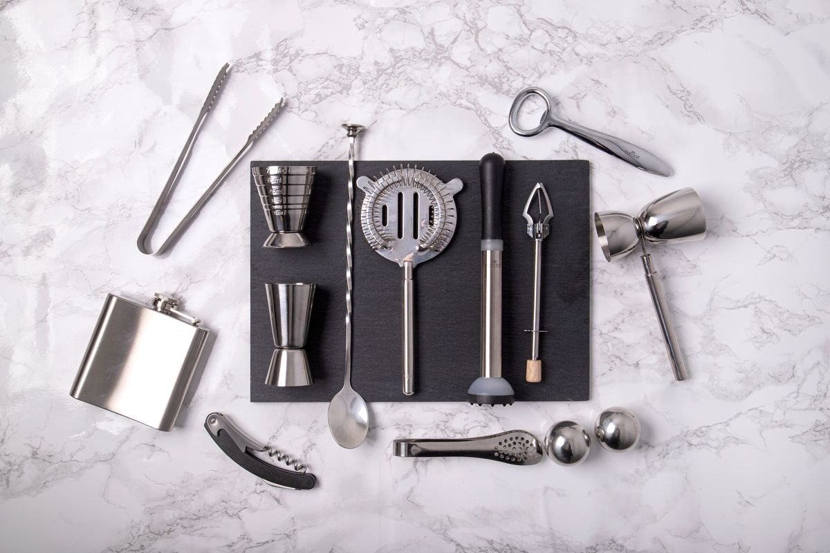 bartender EDC tool kit flat lay with jigger, bottle opener, and hip flask