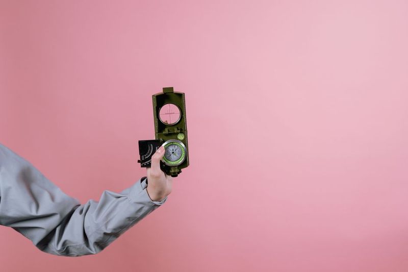 A close-up of a hand holding a compass with a pink background, symbolizing navigation and exploration.