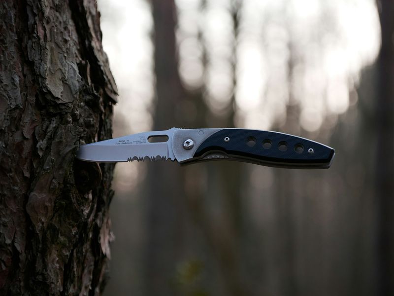 Folding knife blade tested outdoors against tree bark for durability