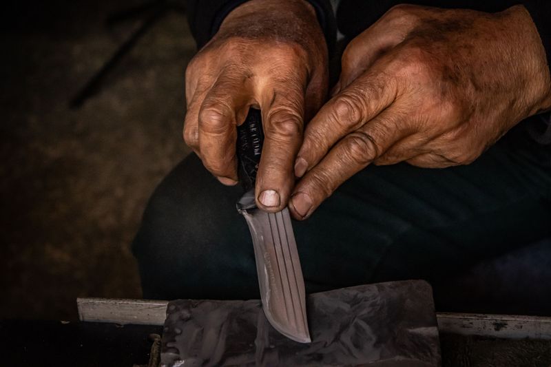 Hands sharpening a pocket knife blade on a whetstone for maintenance