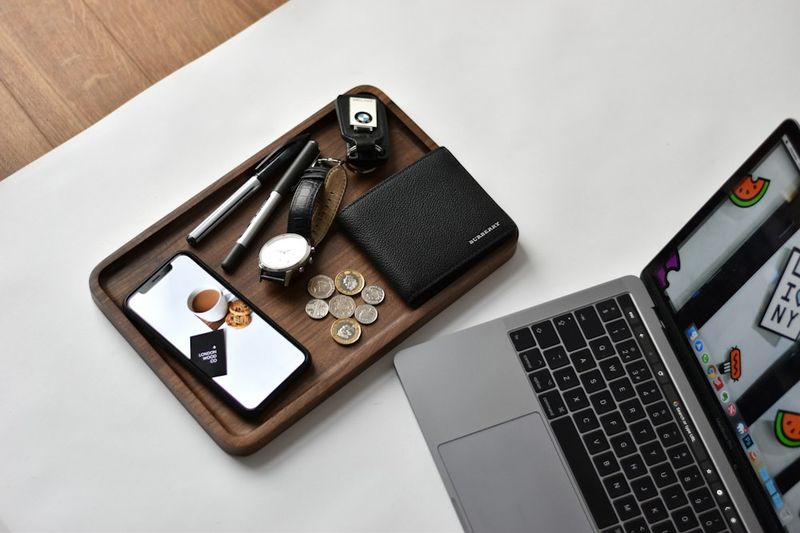 office edc pocket dump with wallet phone watch and pens on a desk tray