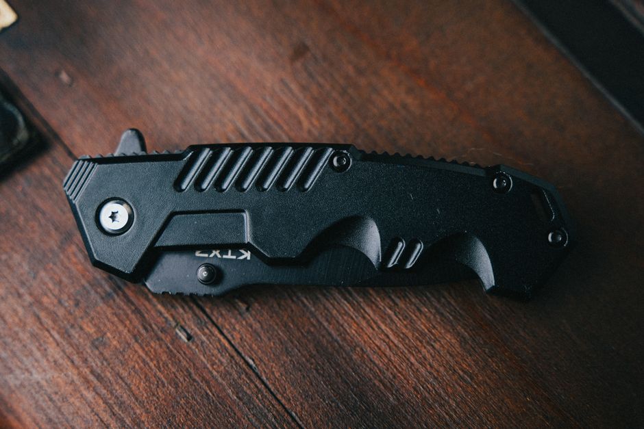Close-up of a black folding knife on a dark wooden surface, showcasing its compact design.